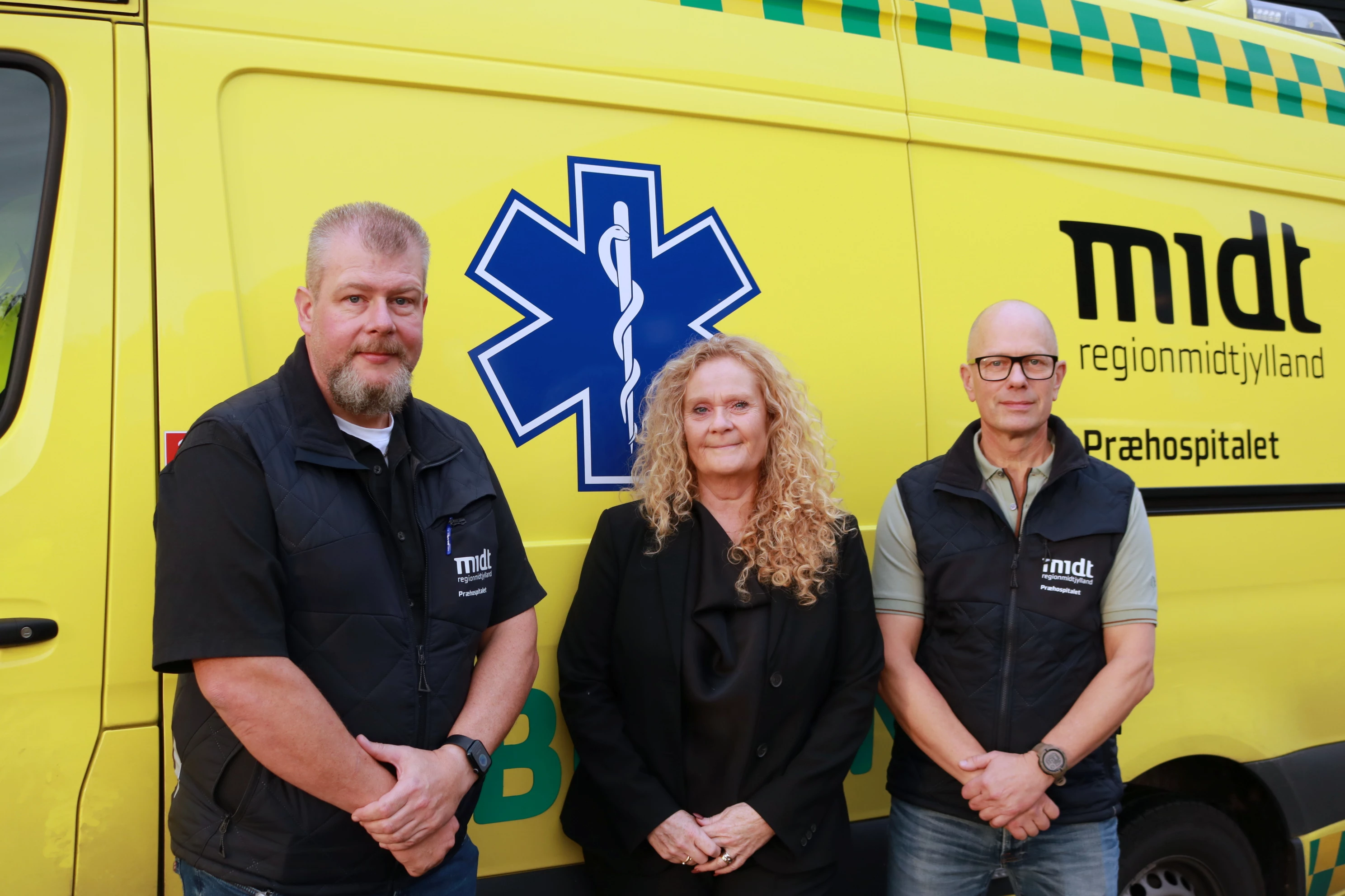 Tre medarbejdere fra Offerrådgivningen står foran en ambulance.